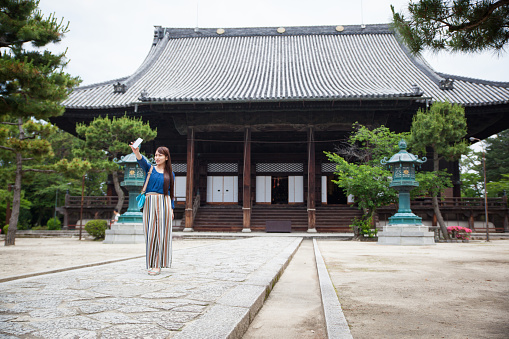 A young Japanese woman takes some photos with her mobile phone of a Buddhist Temple