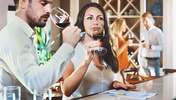 Wine tasting. Closeup of two early 30's people tasting different wine samples at a winery's tasting room. They are writing down their impressions on this red wine. There are blurry people in background, also released wine bar counter stock pictures, royalty-free photos & images
