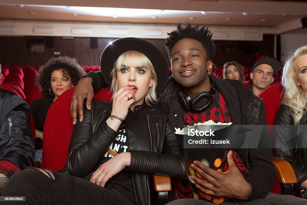 Multi ethnic group of people in the cinema Multi ethnic group of people in the movie theater. Close up of afro american young man holding popcorn in hand, embracing his blonde girlfriend. Movie Theater Stock Photo