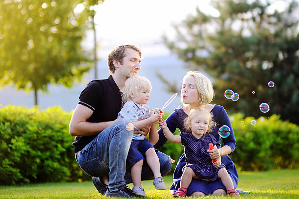 jeune famille avec leurs tout-petits soufflant des bulles de savon - bubble wand outdoors little boys mother photos et images de collection