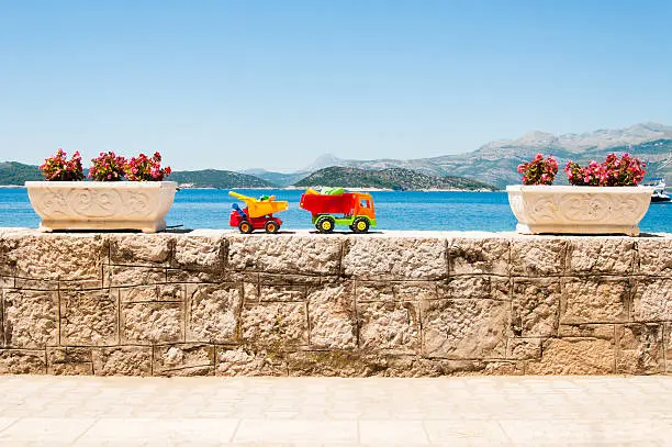 Family vacation concept. Brightly colored kids toy trucks with sea view in the background.