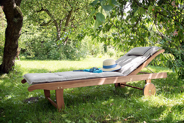 garden daybed of wood on a sunny meadow between trees garden daybed made of wood with hat and sunglasses on a sunny meadow in the orchard, enjoy leisure in nature chaise longue stock pictures, royalty-free photos & images