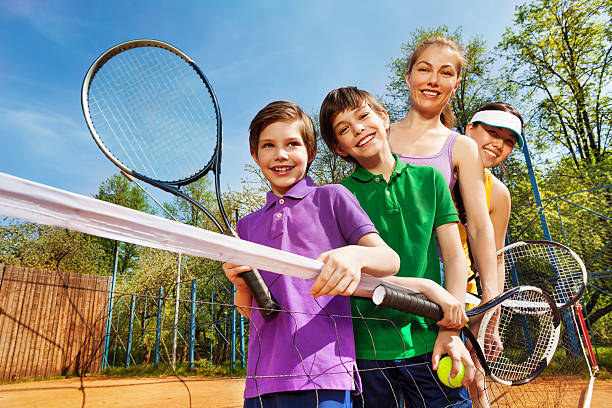 famille de joueurs de tennis debout à côté du filet - tennis child teenager childhood photos et images de collection