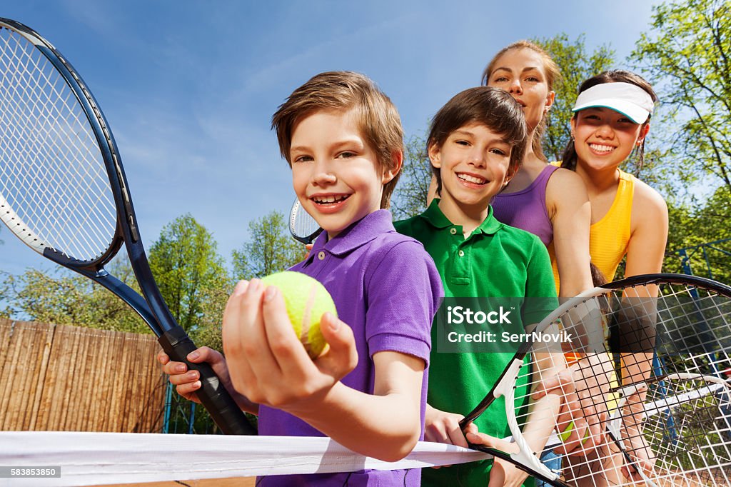 Family playing tennis holding rackets and ball Close-up portrait of smiling active family, holding tennis rackets and ball on the court in sunny day Tennis Stock Photo