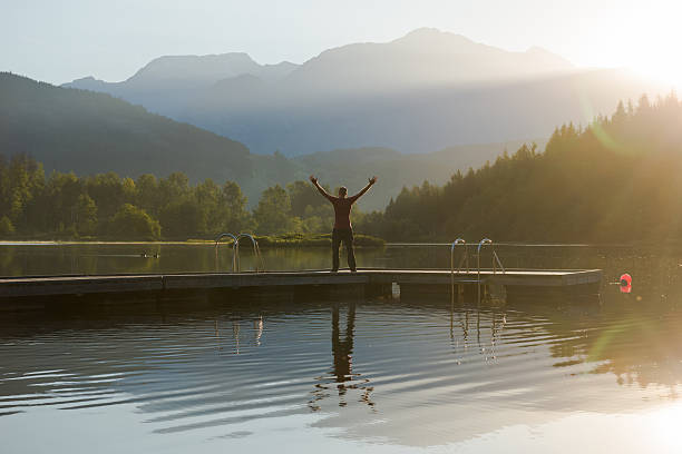 Concept of Success in a natural setting Rejoicing in a stunning natural setting at sunrise. Man raising his arms in victory on a floating dock on a mountain lake. pemberton bc stock pictures, royalty-free photos & images