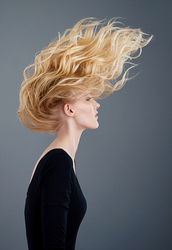 Studio shot of an attractive young woman tossing her beautiful long blonde hair against a gray background