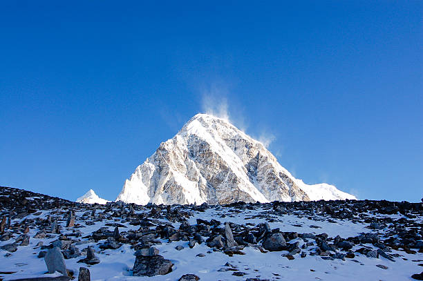 Dark stones spread all over the snowy ground of hillside with Pumori in background on a bright blue sky day.