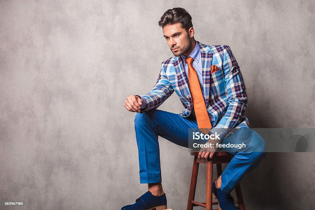 young business man sitting on a chair Side view picture of a young business man sitting on a chair while resting his leg on a wood box. Fashion Stock Photo