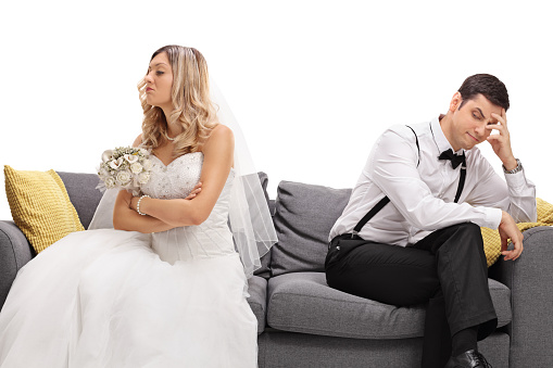 Newlywed coupe sitting on a sofa angry at each other in a middle of an argument isolated on white background