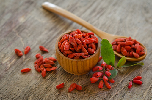 barberries near goji berries heap and wooden spoon, bowl with goji  on wooden background