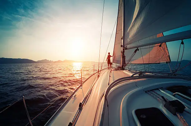 Young man standing on the yacht in the sea at sunset