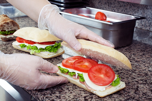 Chef's hands prepare sandwiches in a commercial kitchen