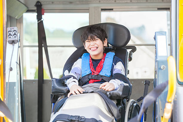 Smiling disabled boy in wheelchair on yellow school bus lift stock photo