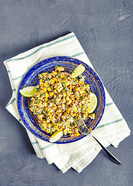 Homemade Mexican Corn Salad Top view vegetarian mexican street food corn salad with cilantro, lime, mayonnaise, garlic, chili and cheese on blue vintage plate on stone background. Sweet, sour and hot tastes from mexican cuisine corn salad stock pictures, royalty-free photos & images
