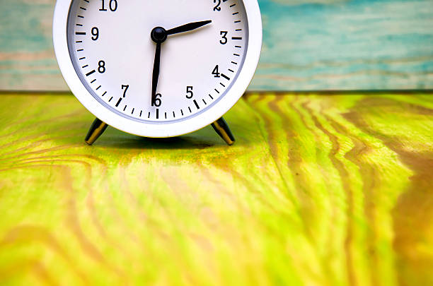 istock White alarm clock isolated on colorful wooden background 583984402