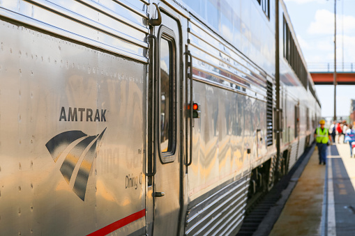Albuquerque, United States - May 24, 2015: The Amtrak passenger train Southwest Chief ready for departure. The doors are closed and a red lamp is flashing, in the back a worker and passengers on the platform.