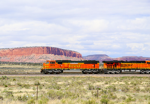 Thoreau, New Mexico, United States - May 24, 2015: Two engines of a BNSF freight train on straight track in the desert in front of rock formations.