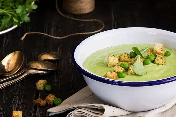 Green spinach and pea soup with croutons. Dark style. Selective focus. Space for text