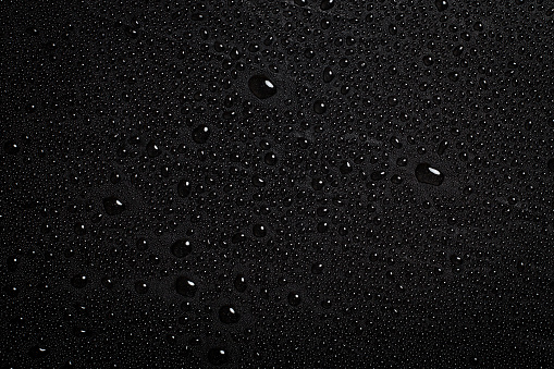 Drops of water on a dark matte surface close up.