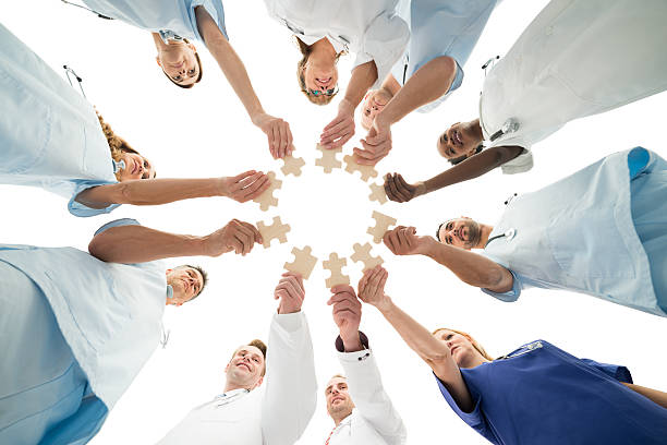 Medical Team Joining Jigsaw Pieces In Huddle Directly below shot of medical team joining jigsaw pieces in huddle against white background jigsaw puzzle photos stock pictures, royalty-free photos & images