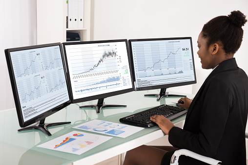 Young African Businesswoman Analyzing Data On Multiple Computer Screen In Office