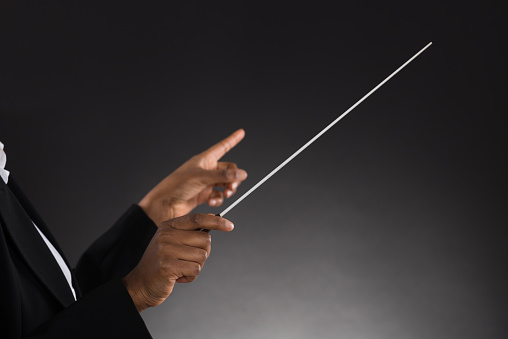 Close-up Of Female Orchestra Conductor Holding Baton Over Black Background