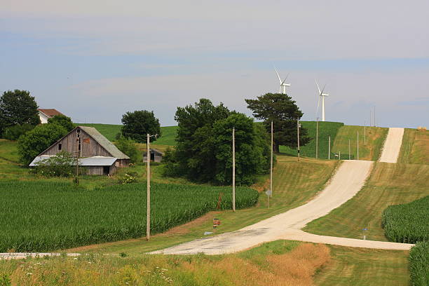 Wind Turbines on the Horizon of an Iowa Gravel Road The gently rolling hills of southwest Iowa are accented with gravel roads, old barns and new wind turbines.  country road road corn crop farm stock pictures, royalty-free photos & images