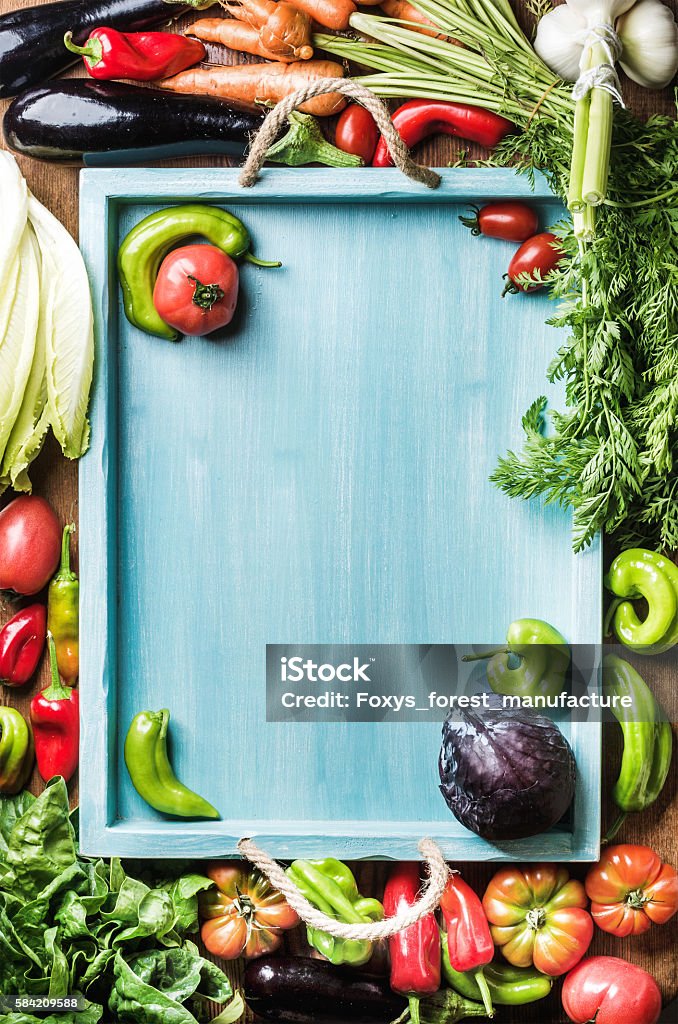 Fresh raw vegetable ingredients for healthy cooking or salad making Fresh raw vegetable ingredients for healthy cooking or salad making on wooden background with blue wooden tray in center, top view, copy space, vertical composition. Artichoke Stock Photo