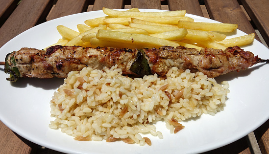 A grilled pork souvlaki skewer with rice and fries