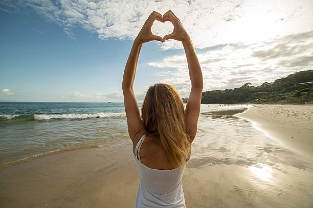 istock Young woman frames beach landscape into heart shape 584218200