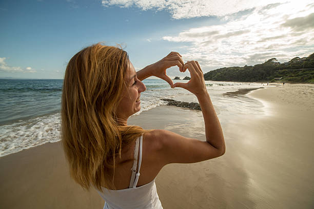 istock Young woman frames beach landscape into heart shape 584218492