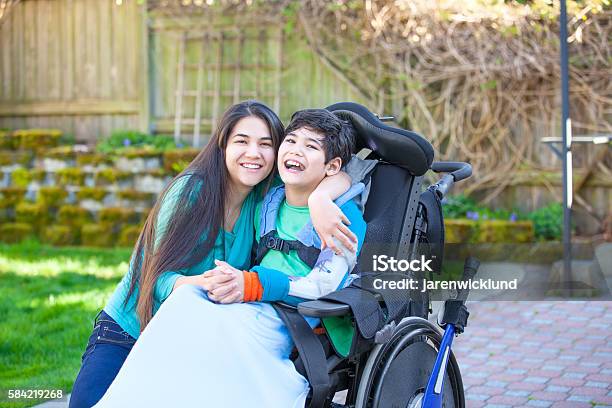 Adolescente Abrazando A Hermano Discapacitado En Silla De Ruedas Al Aire Libre Foto de stock y más banco de imágenes de Niño