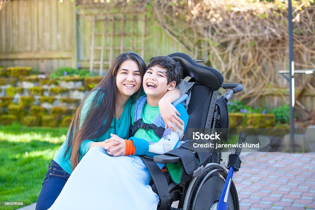Teenage girl hugging disabled brother in wheelchair outdoors Smiling teenage girl hugging disabled nine year old brother in wheelchair outdoors Child Stock Photo