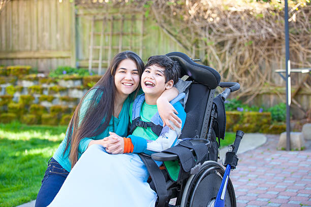 Teenage girl hugging disabled brother in wheelchair outdoors stock photo