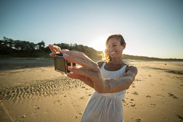 ビーチの女の子はウェアラブルカメラを使用して自分撮りを取ります - australia photographing camera beach ストックフォトと画像
