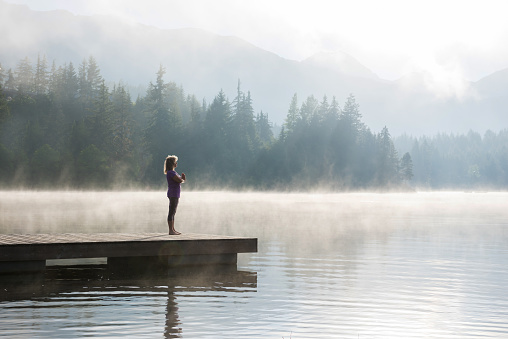Senior woman doing morning yoga at a mountain lake