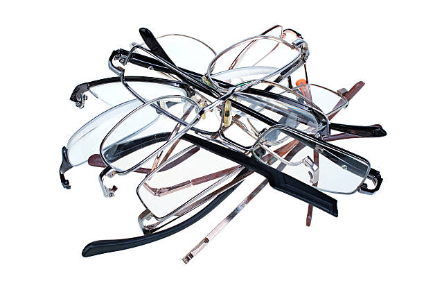 A pair of damaged eyeglasses with one missing lens and another that's heavily scratched and cracked, on a white surface.