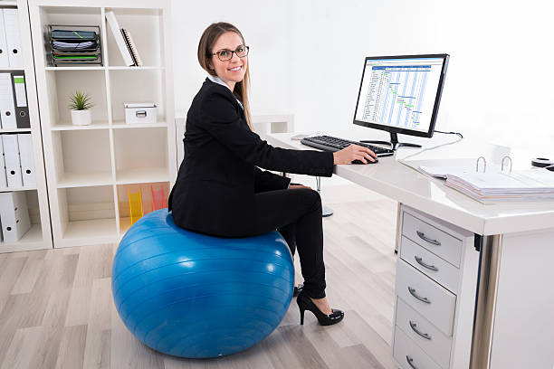 femme d’affaires assise sur un ballon pilates à l’aide d’un ordinateur - photos de fauteuil sphérique photos et images de collection