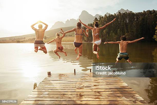 Young Friends Jumping Into Lake From A Jetty Stock Photo - Download Image Now - Lake, Jumping, Diving Into Water