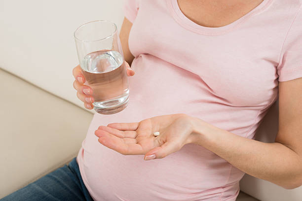 mão de mulher grávida com copo de água e pílula de vitamina - ácido fólico - fotografias e filmes do acervo