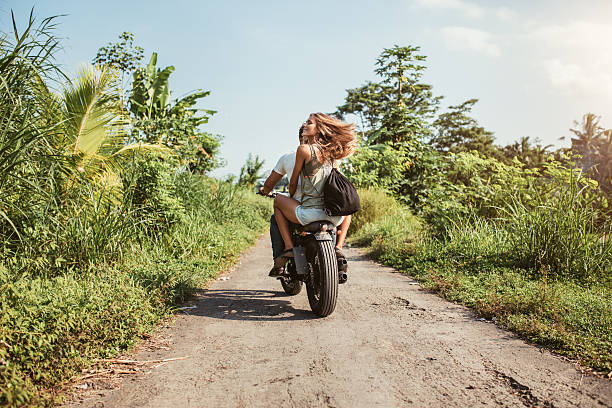 Rear view of young couple riding motorcycle on rural road. Woman with her boyfriend riding on motorbike on a summer day.