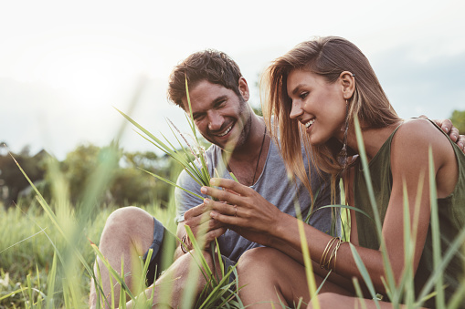Couple sitting in a field of grass. Man and woman together with wild grass in hand.