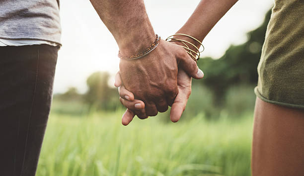 giovane coppia tenendo le mani sul campo - holding hands human hand holding couple foto e immagini stock