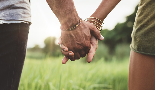 Young couple walking through meadow hand in hand. Close up shot with focus on hands of man and woman.