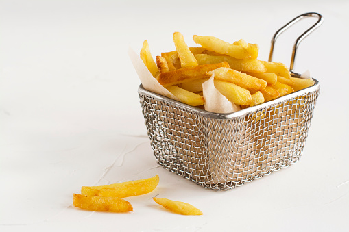 French fries in metal wire basket over white kitchen table. Selective focus