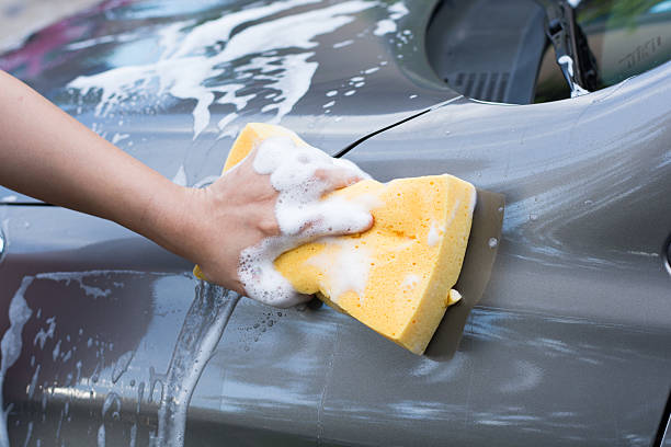istock Female hand with yellow sponge washing car 584237082