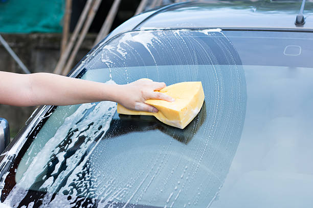 istock Female hand with yellow sponge washing car 584237400