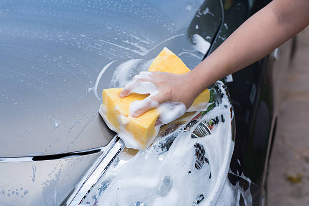 istock Female hand with yellow sponge washing car 584237484