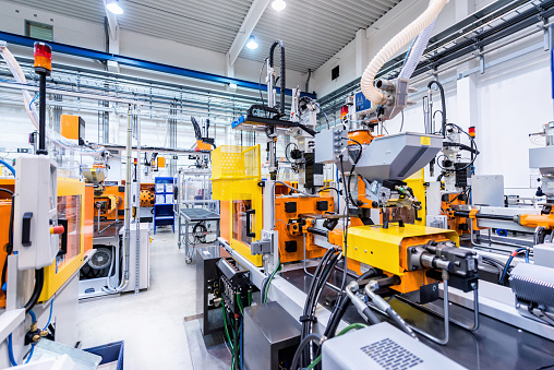 Horizontal color image of large group of automated injection moulding machines for plastic parts production. Powerful molding machinery in factory arranged in a row.