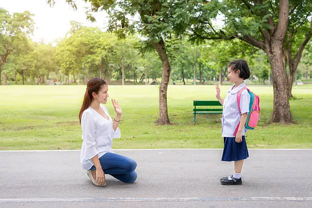 Back to school. Asian mother say goodbye to daughter student in park at school before study. Asian mother sent hand sign to goodbye.